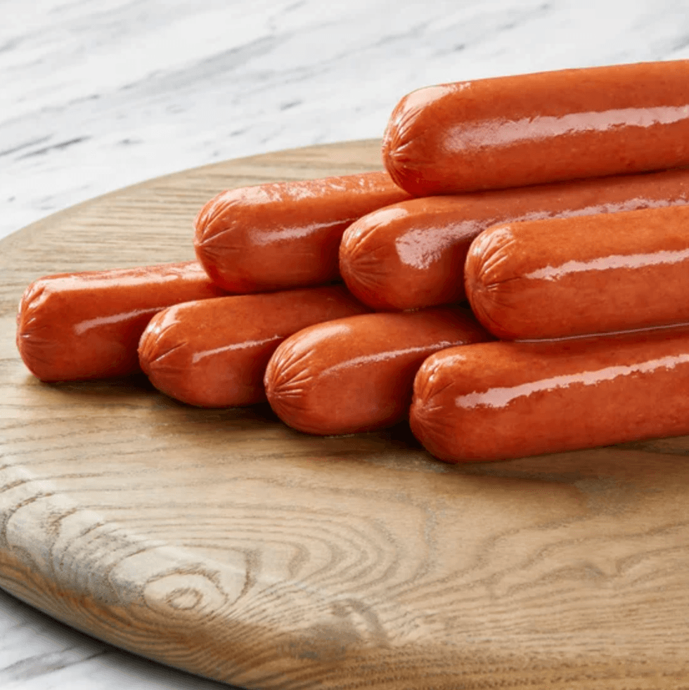 Stack of uncooked hot dogs on a round wooden board.