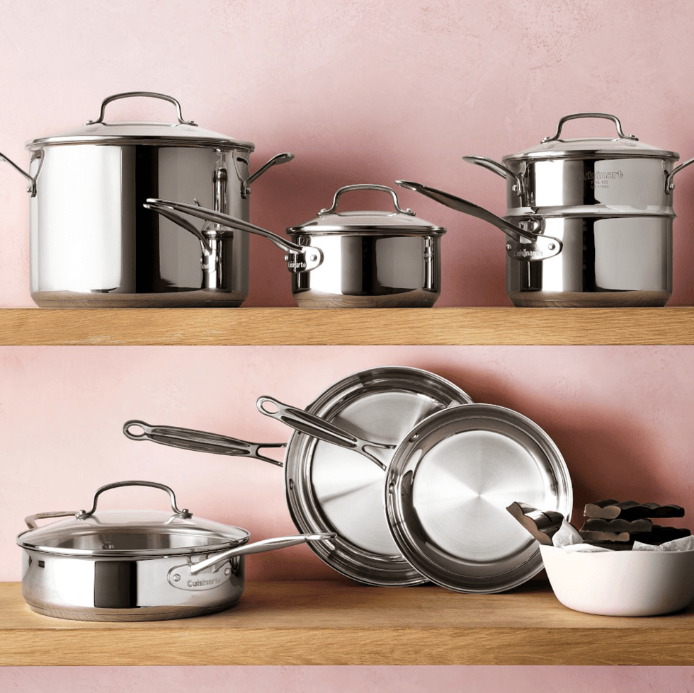Stainless steel cookware set on wooden shelves against a pink wall.