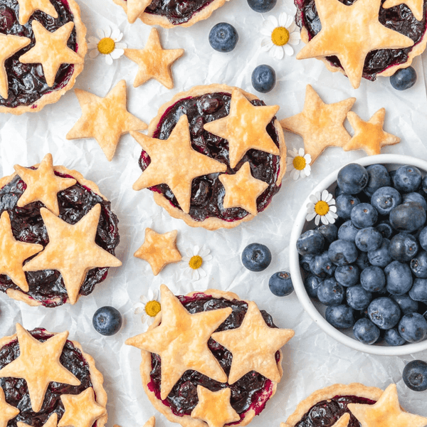 Star-shaped blueberry tarts with fresh blueberries on a textured surface.