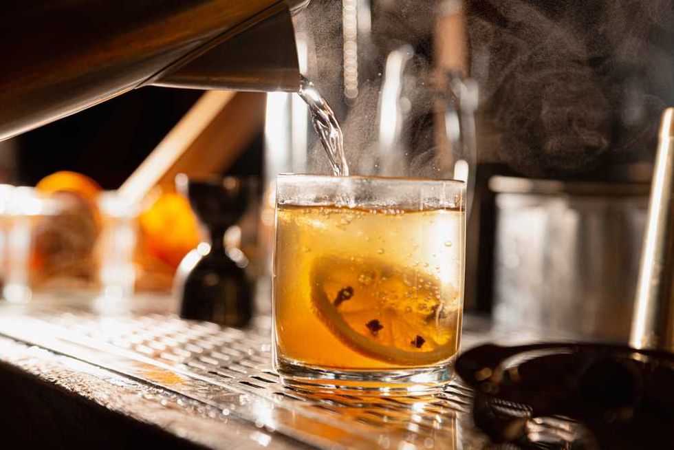 Steaming cocktail with citrus slice poured in glass on a bar counter.