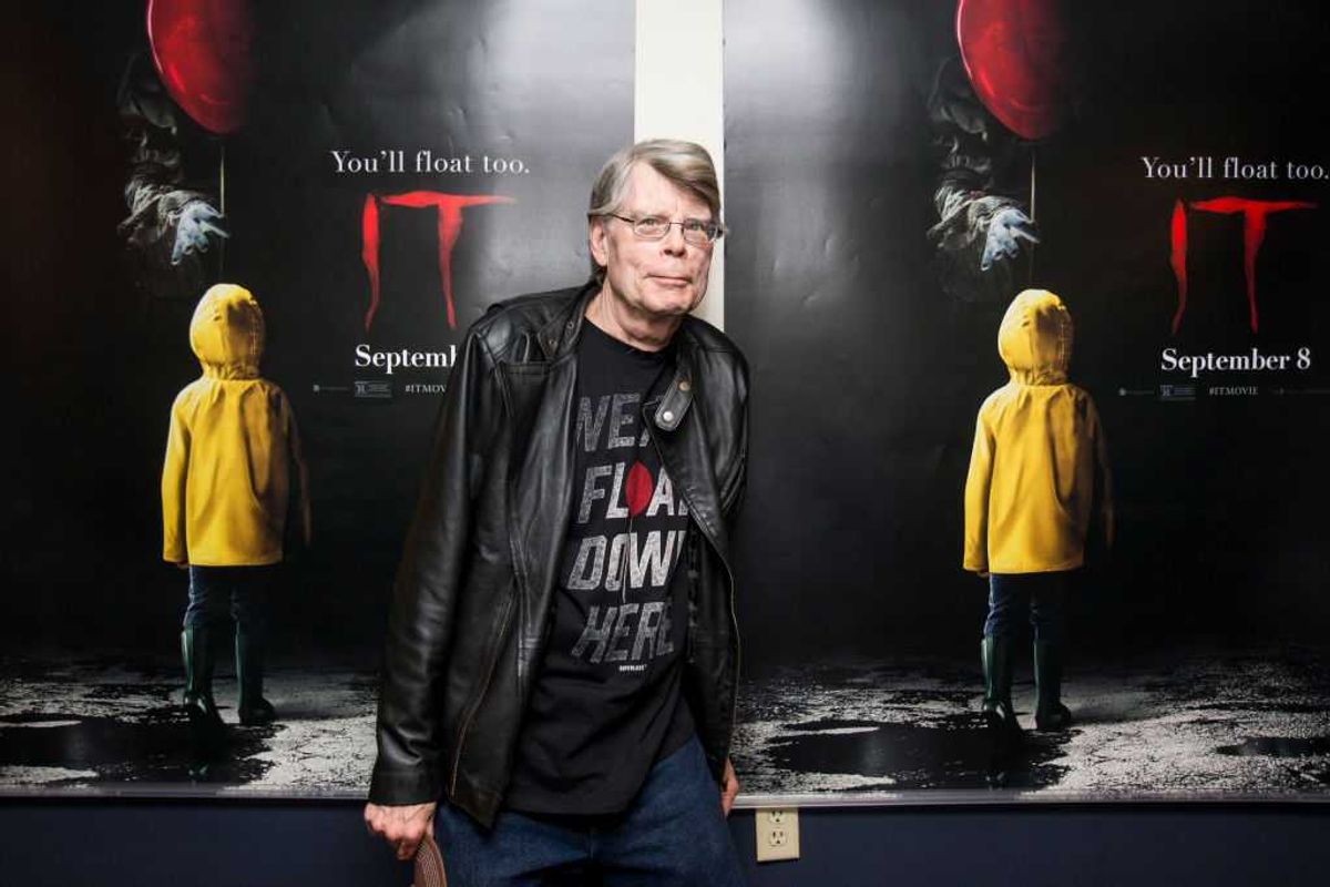 Stephen King standing between two "IT" movie posters featuring a child in a yellow raincoat.