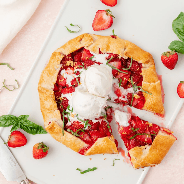 Strawberry galette with ice cream, garnished with basil, on a white plate.