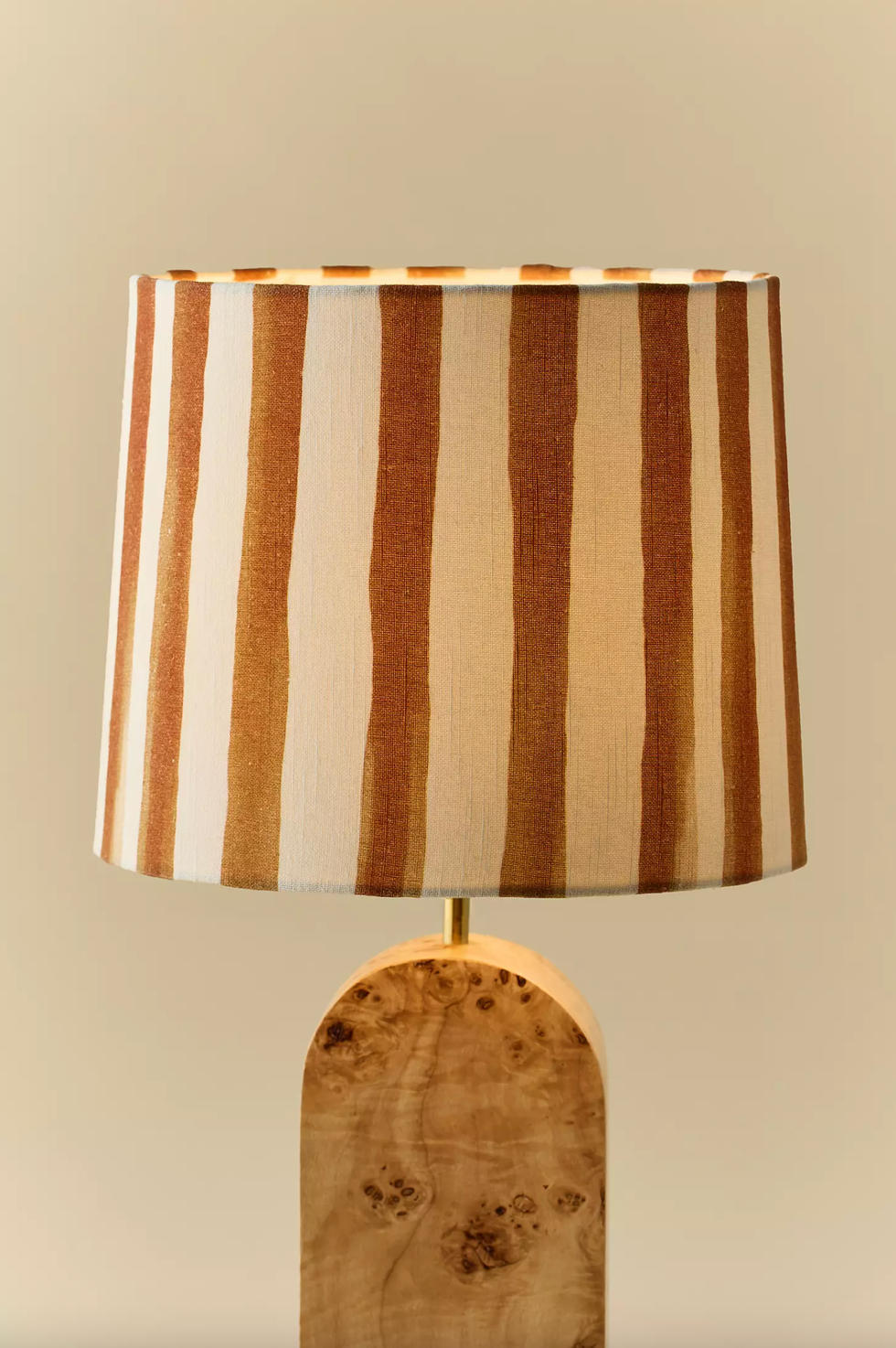 Striped lamp with a natural wood base against a beige background.