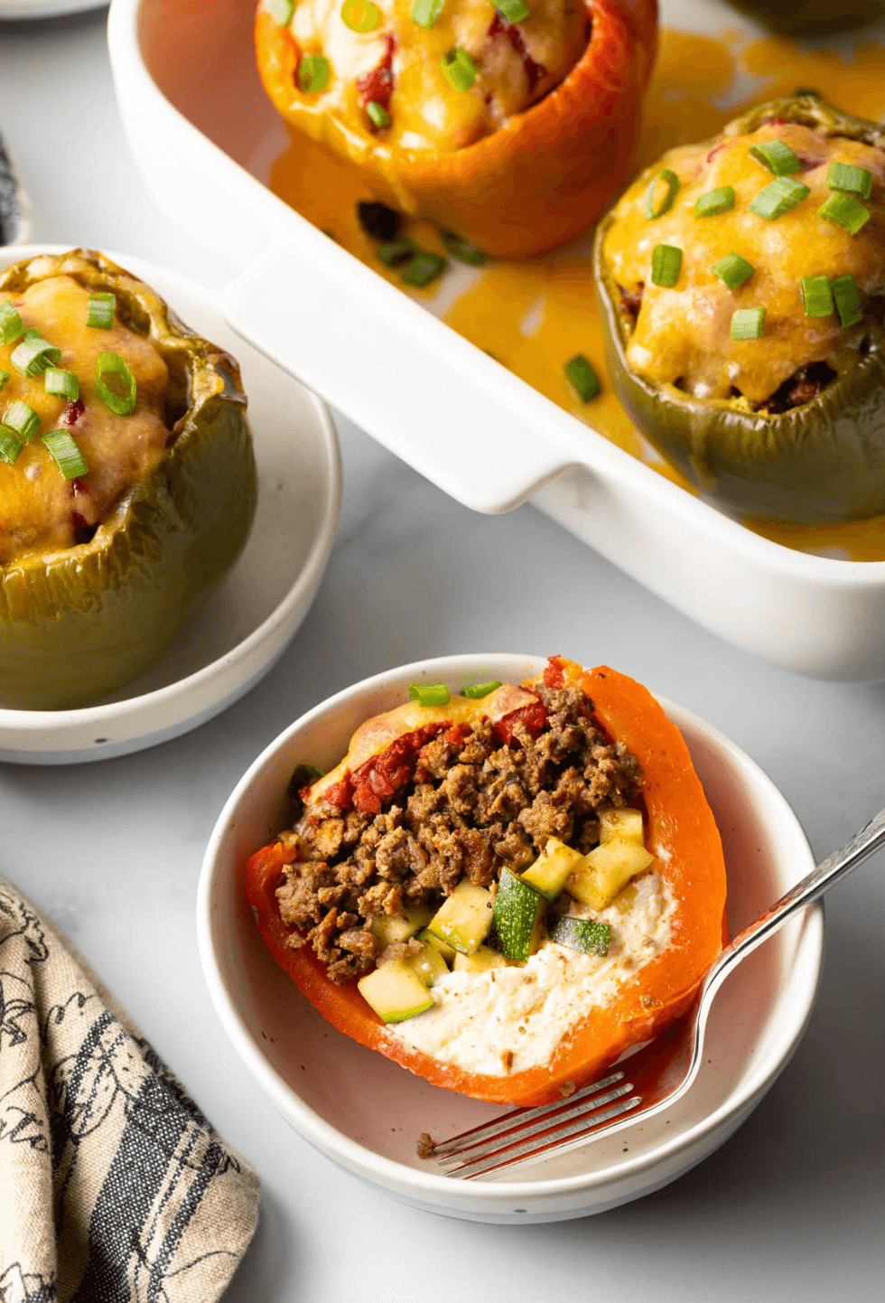 Stuffed peppers with beef, zucchini, cheese, topped with green onions on a dish.