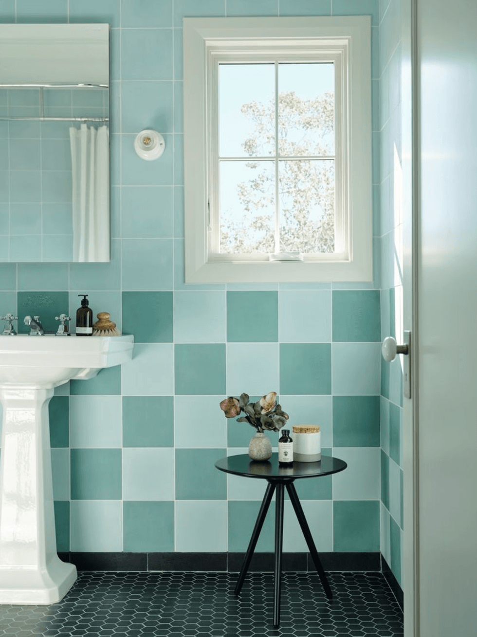 Stylish bathroom with blue tiles, pedestal sink, and decorative table by a window.