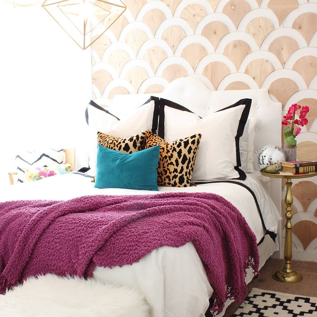 Stylish bedroom with a purple throw, leopard pillows, and gold accents against a patterned wall.
