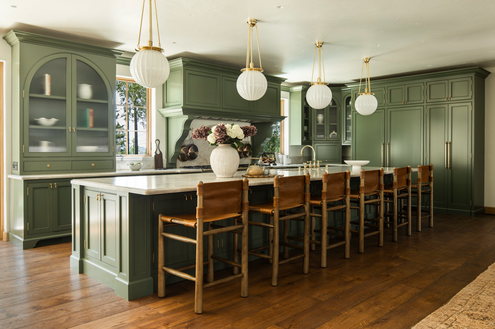 Stylish kitchen with green cabinetry, marble island, leather chairs, and pendant lights.