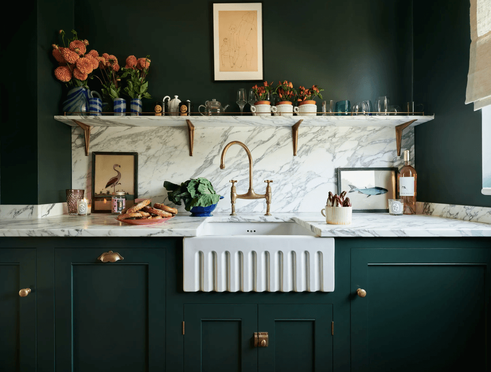 Stylish kitchen with marble counters, green cabinets, and copper faucet.