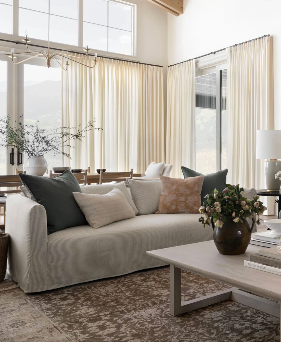 Stylish living room with a sofa, decorative pillows, large windows, and a wooden coffee table.