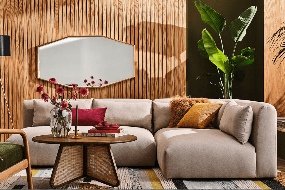 Stylish living room with beige sofa, round table, wall mirror, and tropical plant.
