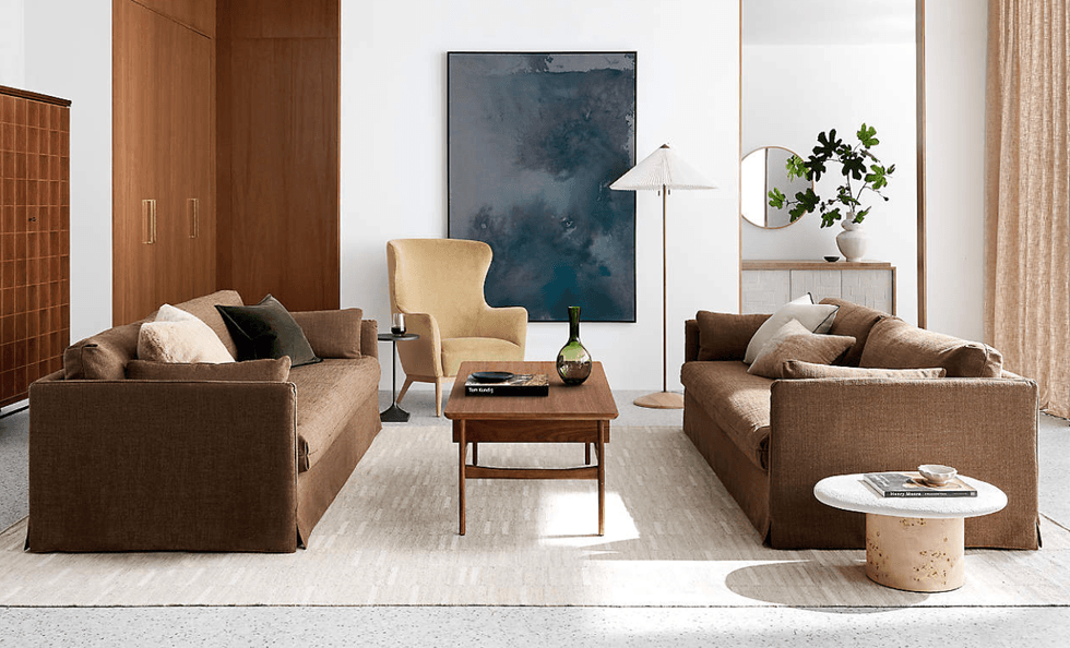 Stylish living room with brown sofas, a yellow chair, art, and plants in a modern setting.