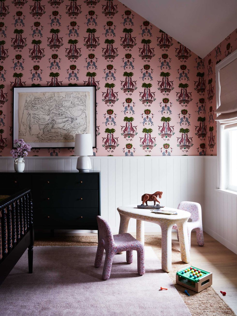 Stylish nursery with pink patterned wallpaper, play table, and toy horse on the wall.