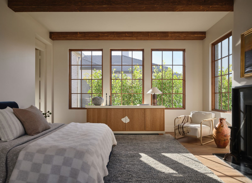 Sunlit bedroom with wooden beams, checkered bedding, and large windows overlooking greenery.