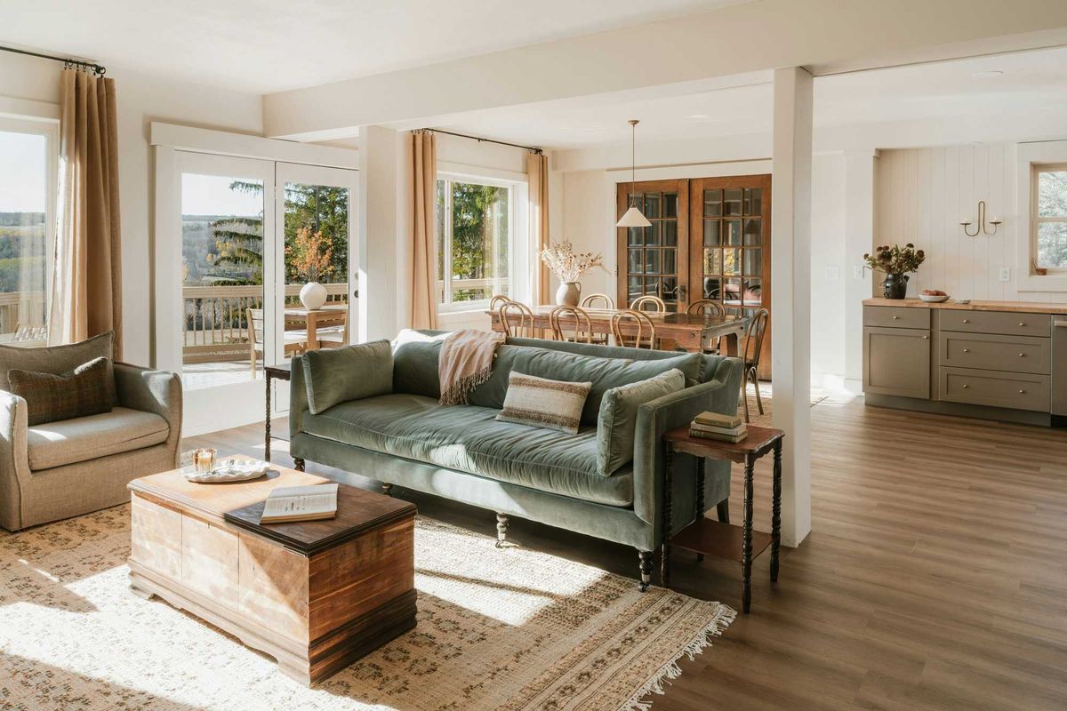 Sunlit living room with green sofa, wooden coffee table, and dining area in the background.