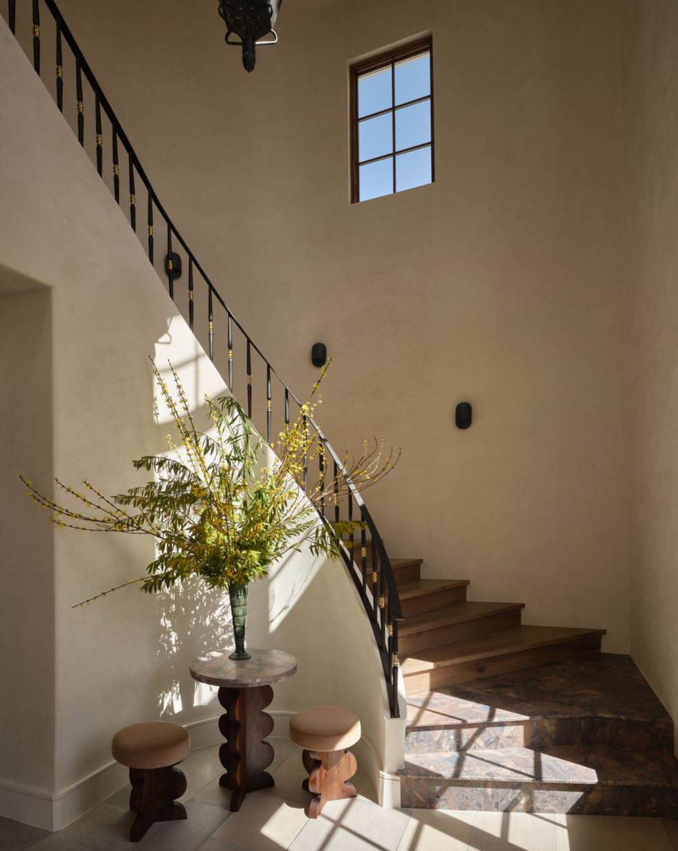 Sunlit staircase decor with floral vase and round stools in a modern interior.