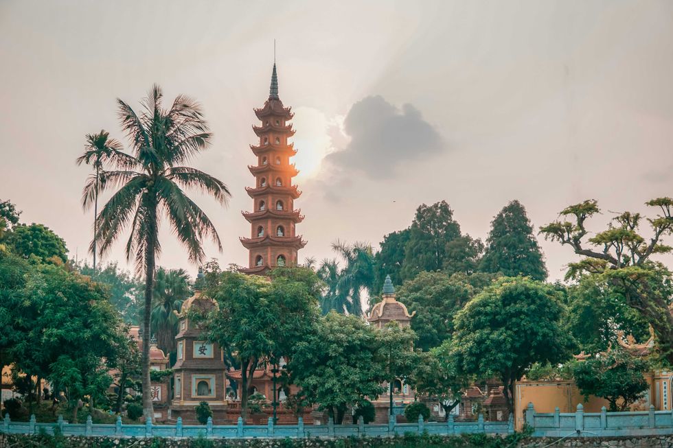 Sunset over a pagoda surrounded by palm trees and lush greenery.