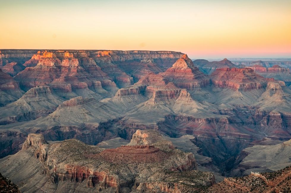 Sunset over the Grand Canyon; vast, colorful rock formations under a glowing sky.