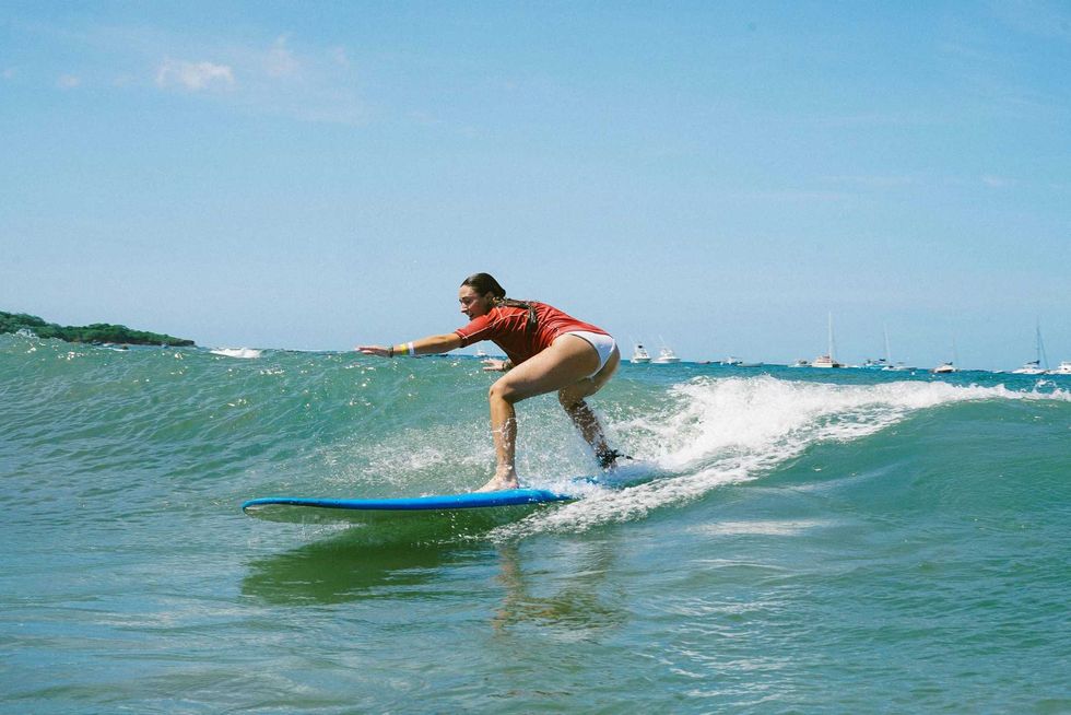Surfer riding a wave on a blue surfboard with boats in the background.