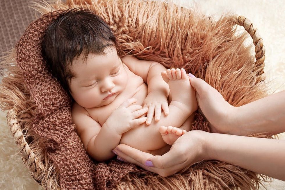 Sweet newborn baby sleeps in basket. Newborn baby in mother hands. Mother holding legs of the kid in hands. Happy family concept.