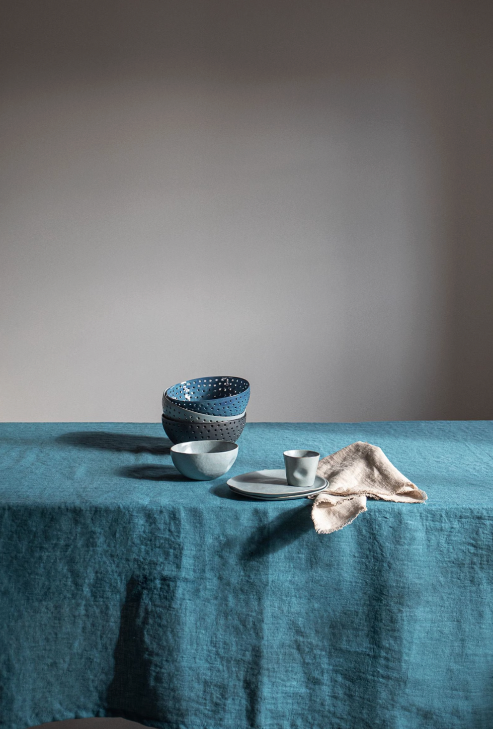 Table with stacked bowls, cup, saucer, and beige cloth on a blue linen tablecloth.