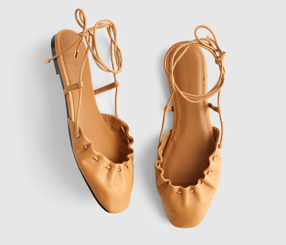 Tan leather ballet flats with lace-up straps on a white background.