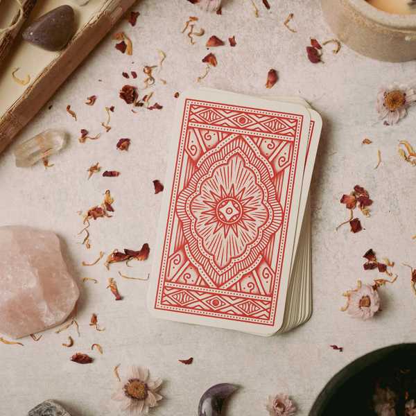 Tarot cards with red patterns on a table surrounded by crystals and dried flowers.