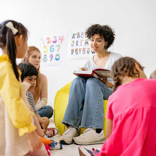 Teacher reading to attentive children seated in a circle, with alphabet posters on the wall.