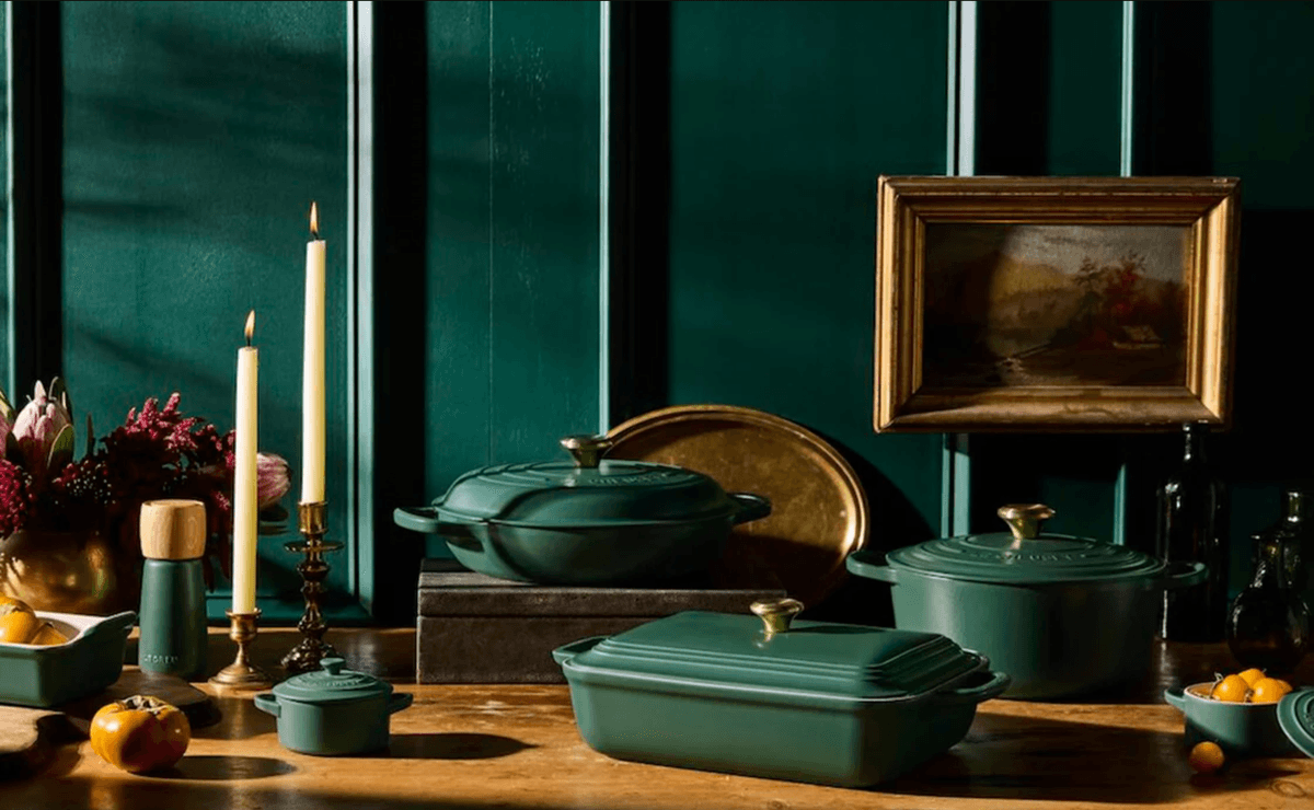 Teal cooking pots, candles, and art against dark green paneled wall on wooden table.
