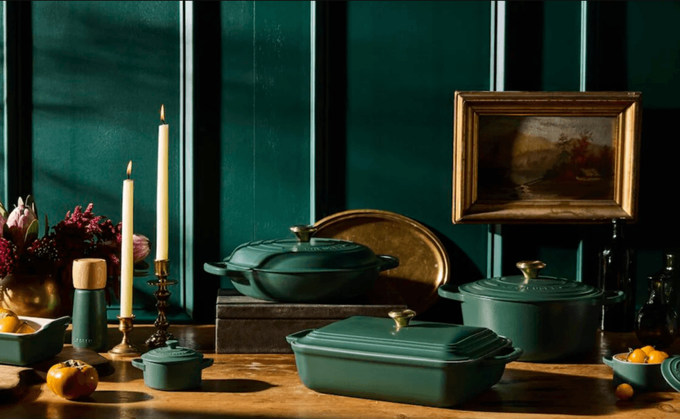 Teal cooking pots, candles, and art against dark green paneled wall on wooden table.