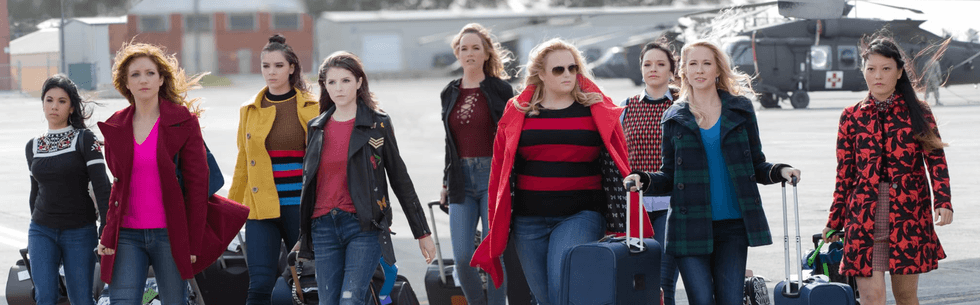 Ten women with suitcases walking on an airfield beside helicopters.