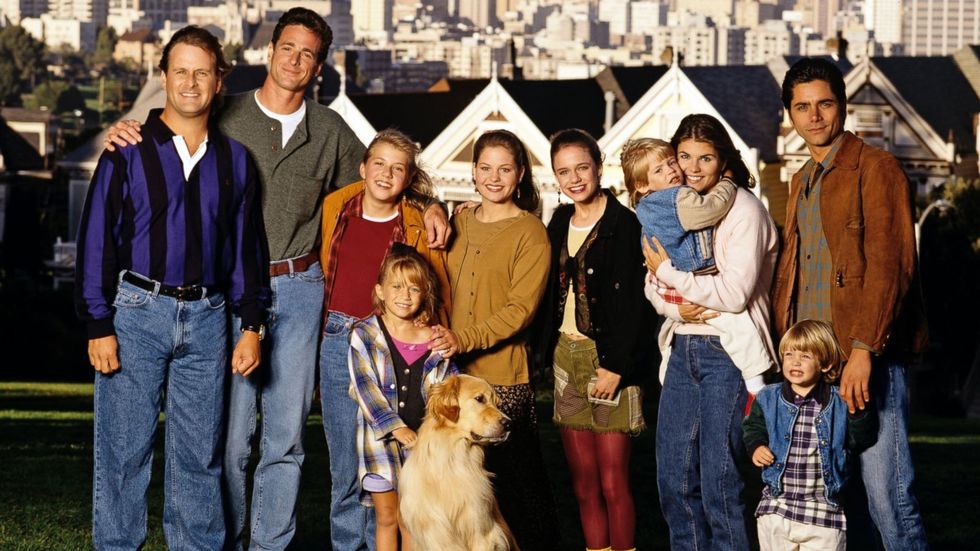 The cast of Full House smiles for a picture in front of houses in San Francisco.