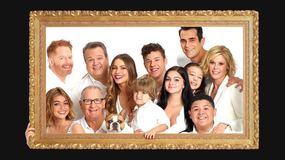 The cast of Modern Family is posing behind a wooden picture frame.