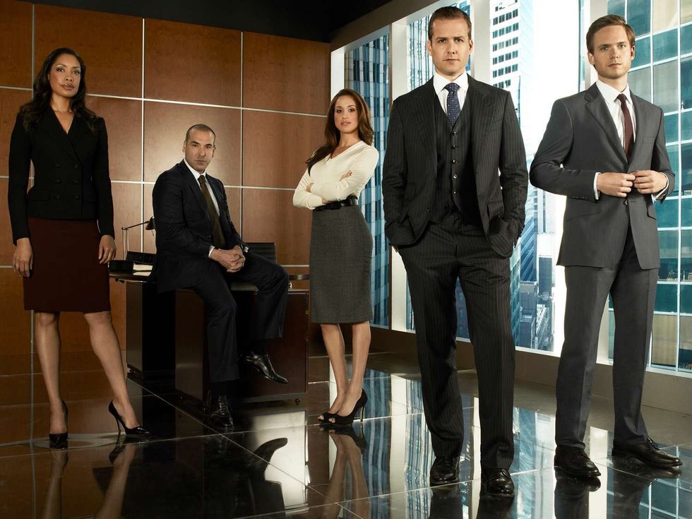 The cast of Suits pose in business attire in the office.
