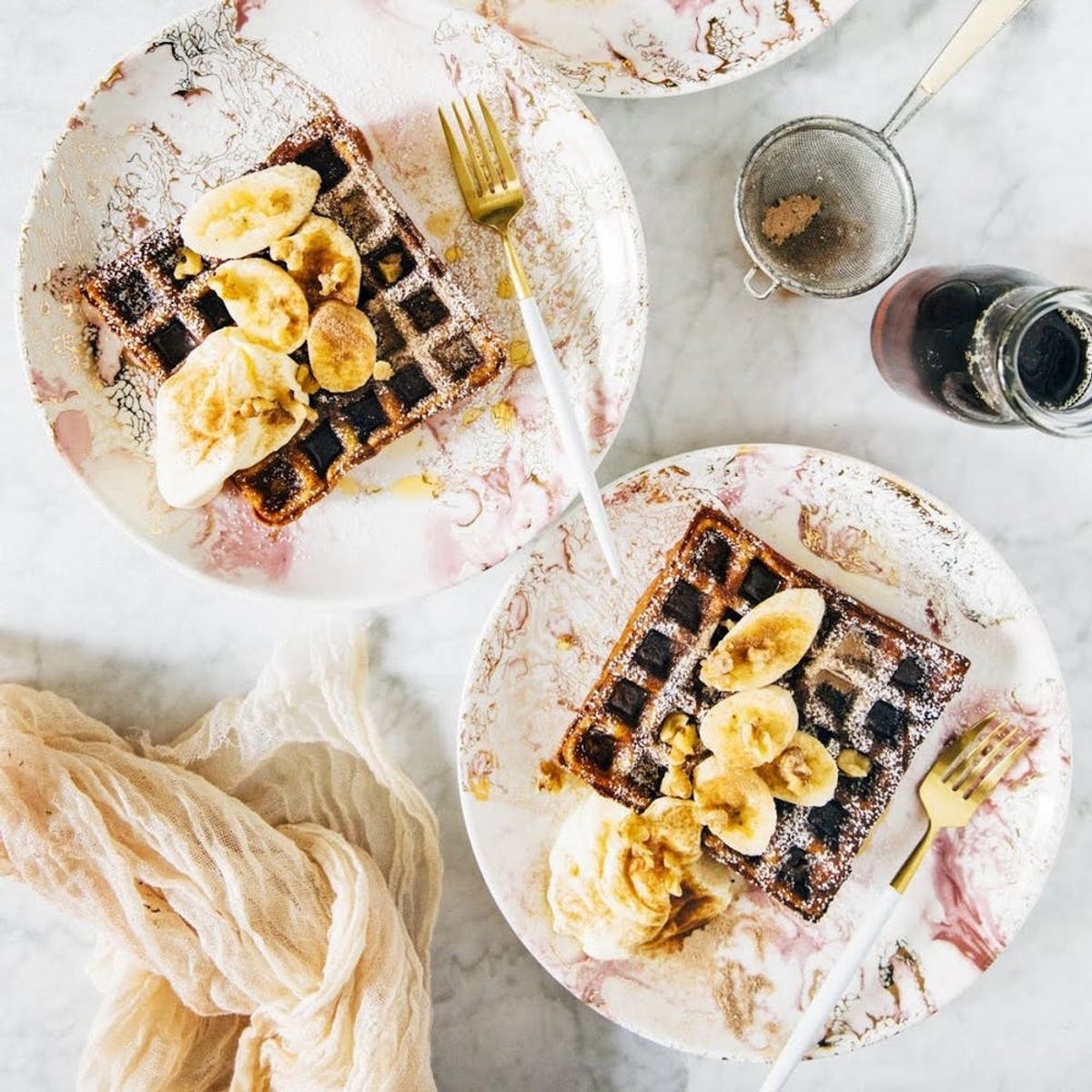 This waffle paleo breakfast rests on a white plate with chocolate sauce, bananas, and whip cream