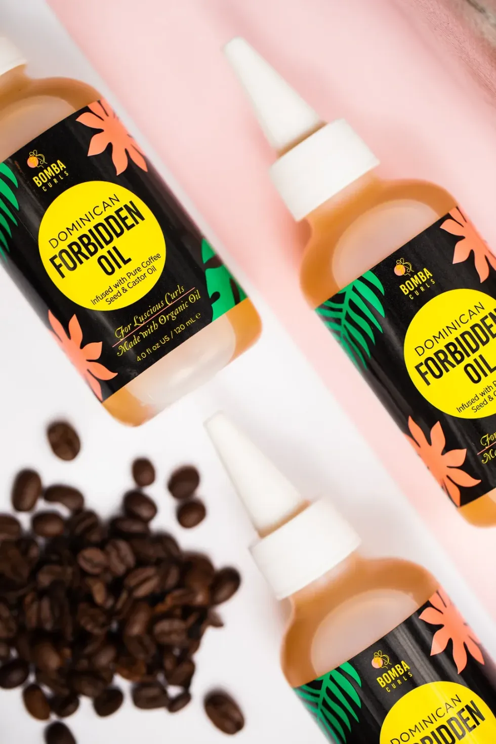 Three bottles of the Bomba Curls Dominican Forbidden oil are next to coffee beans.