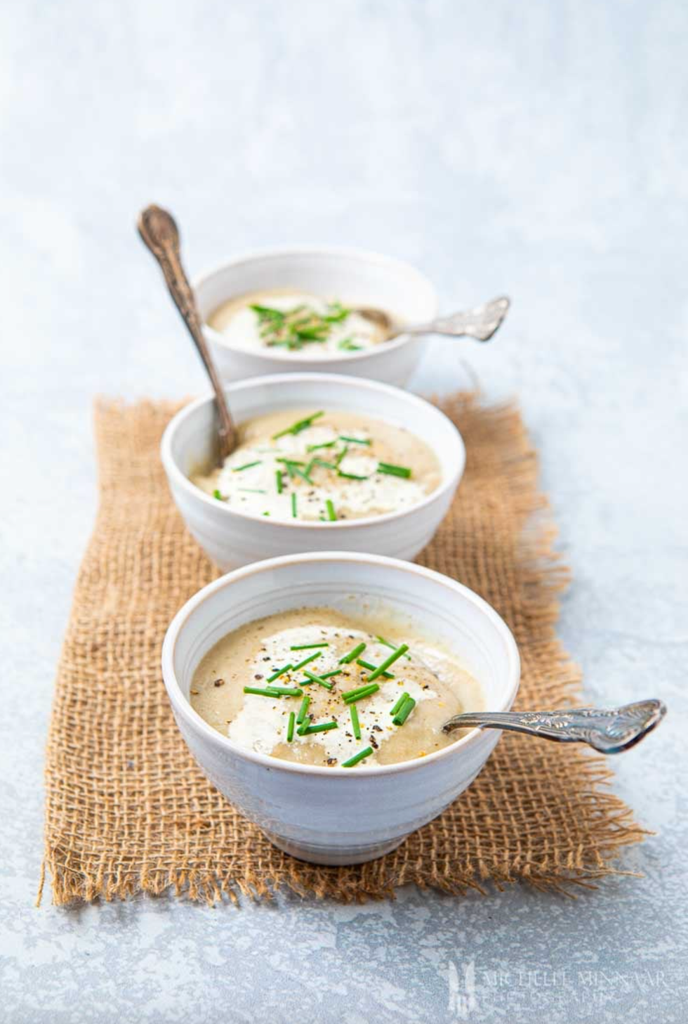 Three bowls of creamy soup topped with chives and black pepper on a burlap mat.