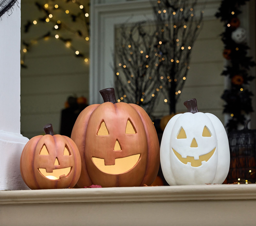 Three carved pumpkins on steps, two orange and one white, with glowing lights inside.