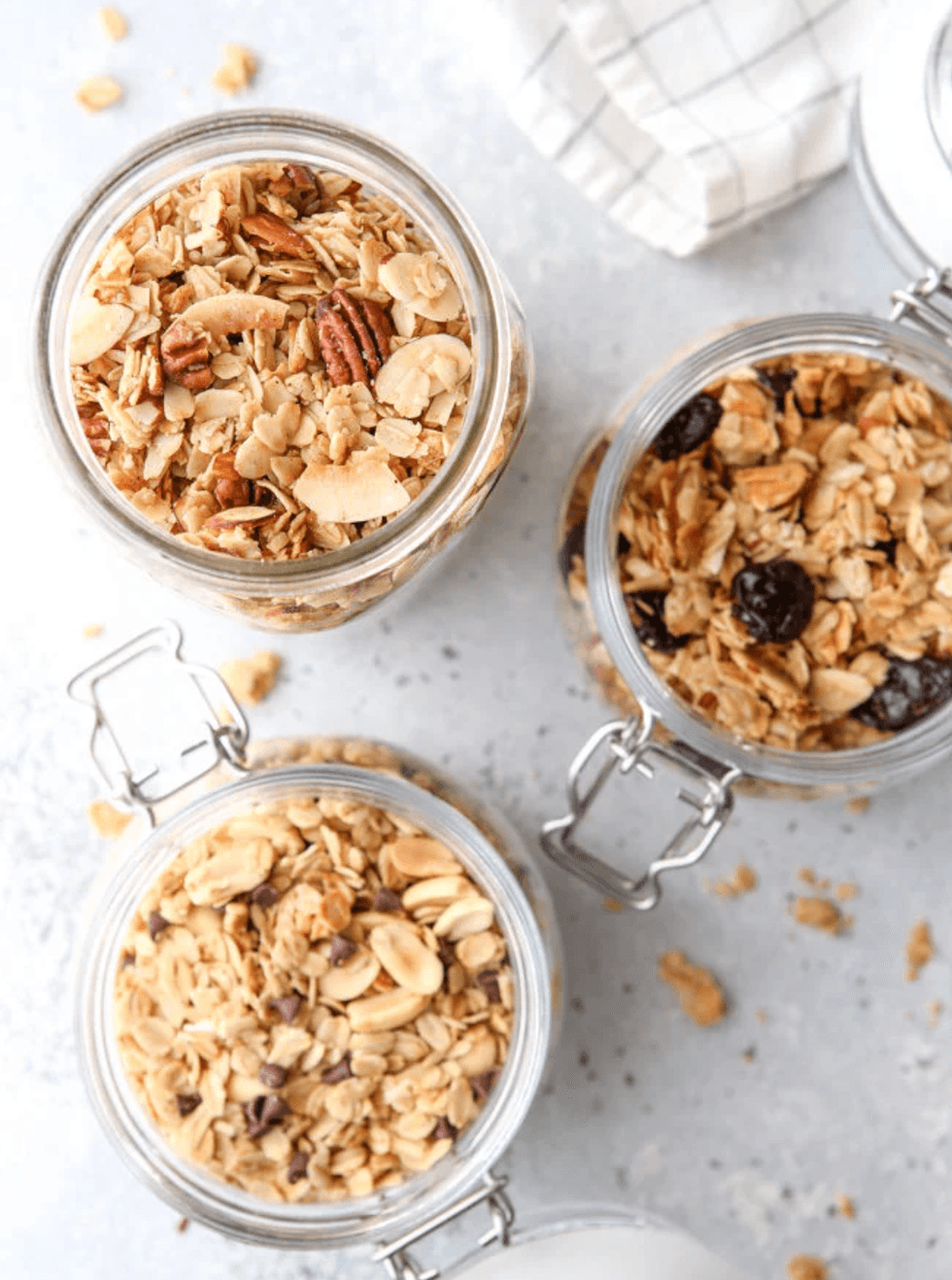 Three glass jars filled with assorted granola on a light gray surface.