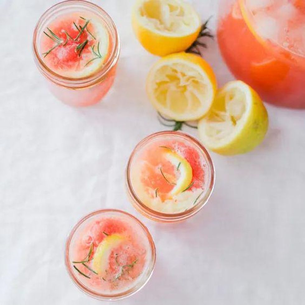 Three glasses of pink lemonade with lemon slices and rosemary, next to squeezed lemons.