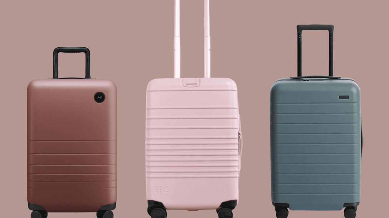 Three hard-shell suitcases in brown, pink, and teal on a matching background.