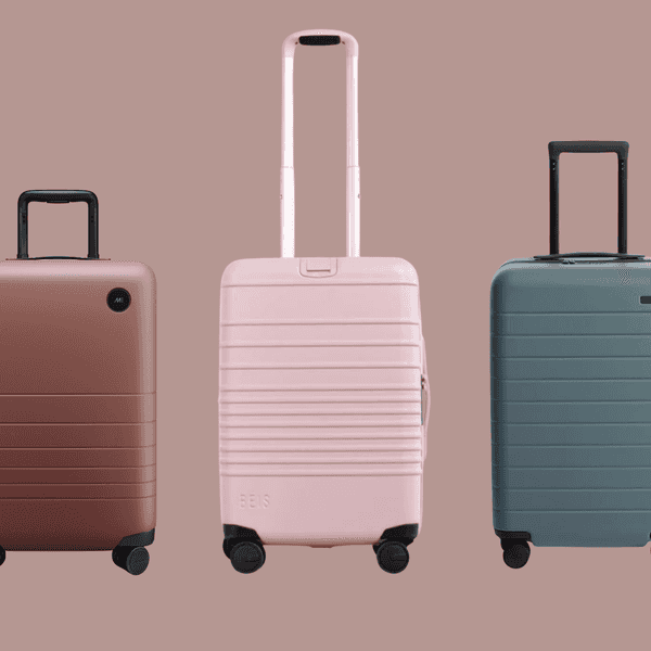 Three hard-shell suitcases in brown, pink, and teal on a matching background.