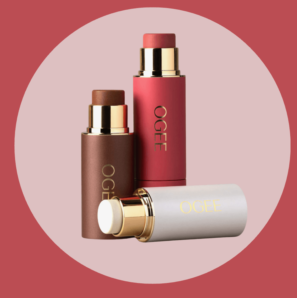 Three Ogee multi-use stick cosmetics in red, brown, and white on a circular pink background.