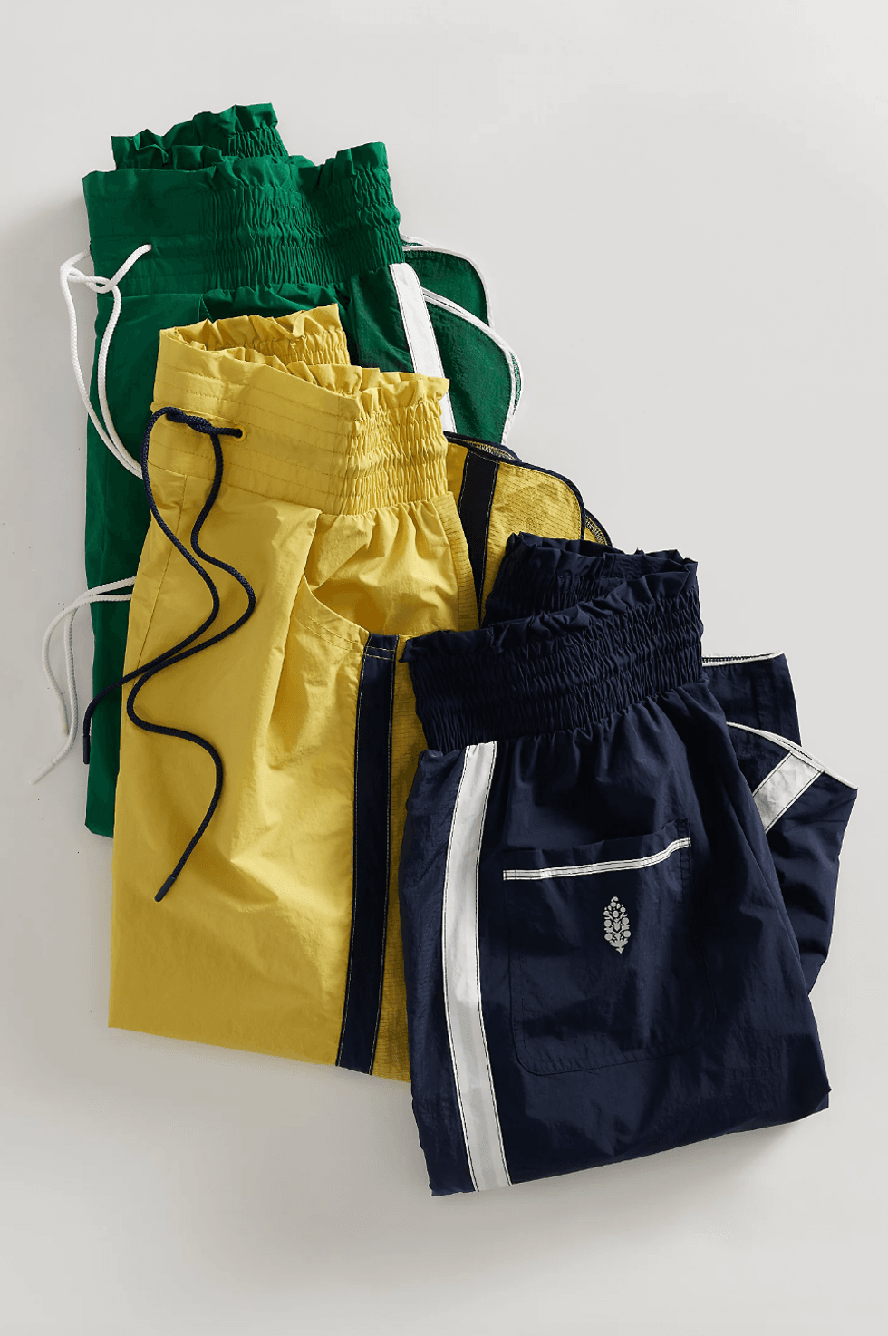 Three pairs of colorful boxer shorts: green, yellow, and navy blue with drawstrings.