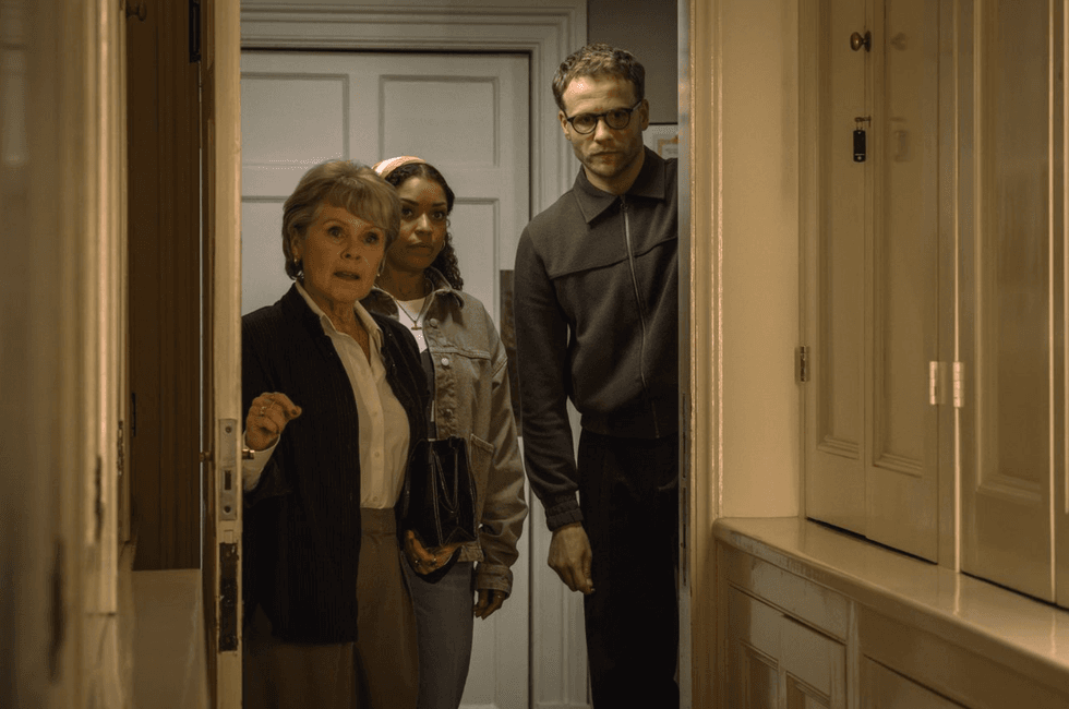 Three people cautiously enter a dimly lit room, looking slightly apprehensive.