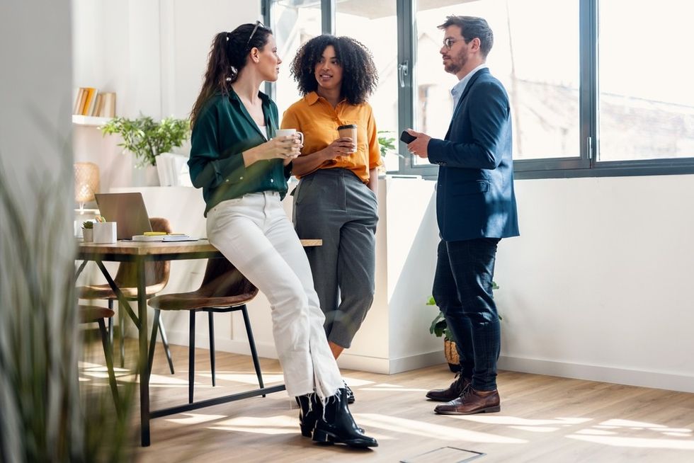 Three people chatting with coffee in a bright, modern office space.