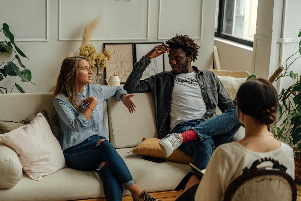 Three people having a discussion in a cozy, plant-filled living room.