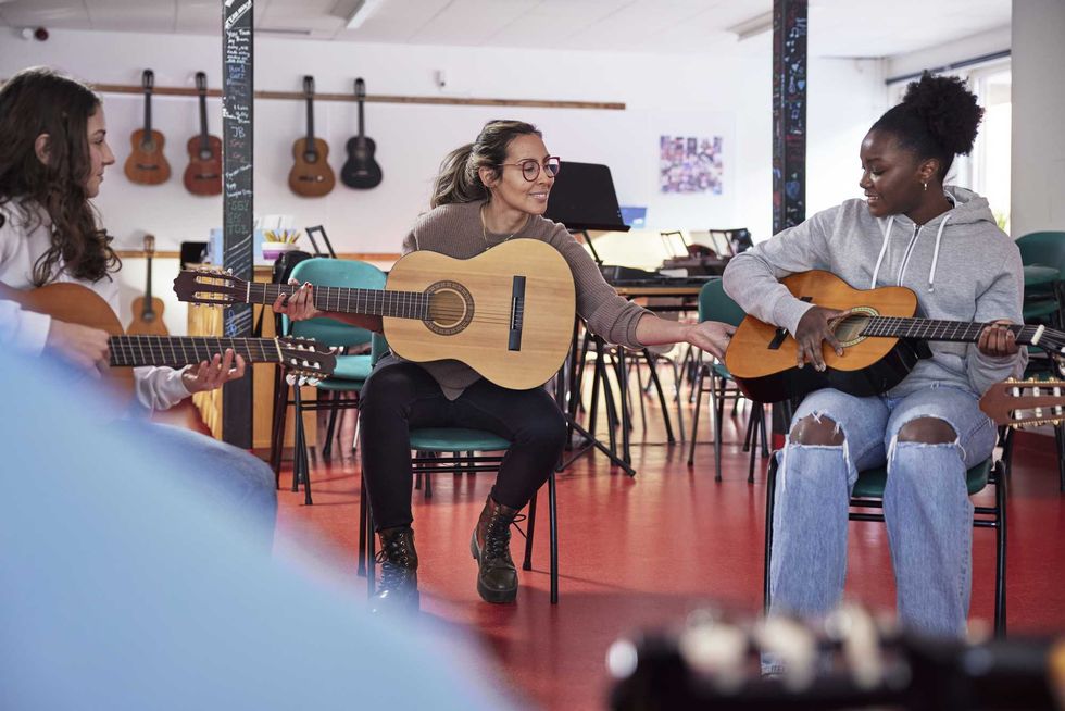 Three people in a music class playing guitars and smiling at each other.