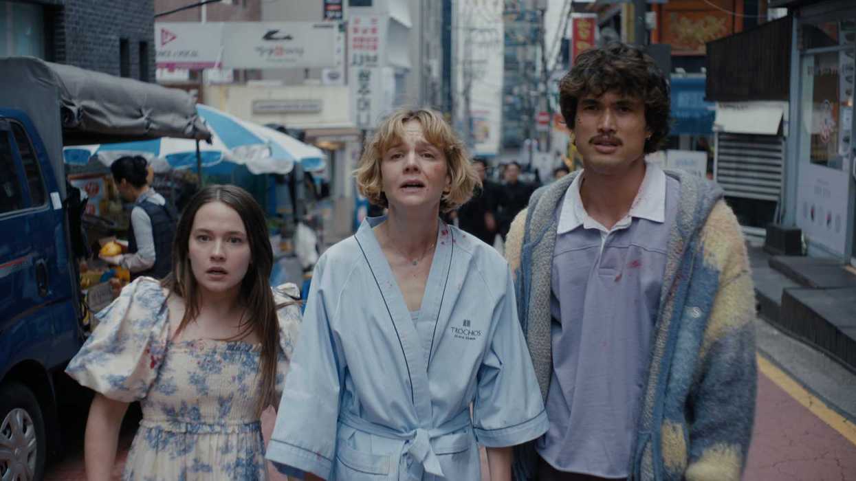 Three people in casual clothing walking down a busy urban street with signs and a market stall.