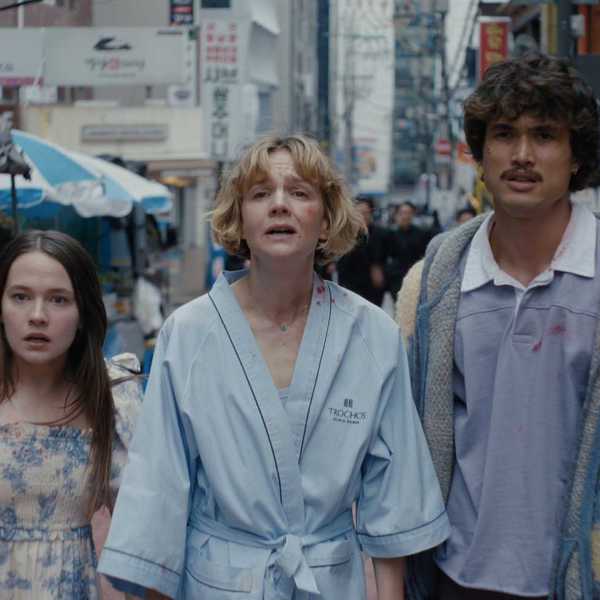 Three people in casual clothing walking down a busy urban street with signs and a market stall.