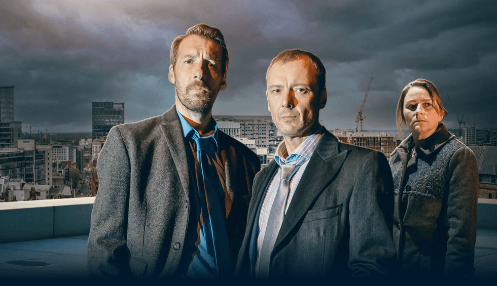 Three people in suits stand on a rooftop with a moody cityscape background.